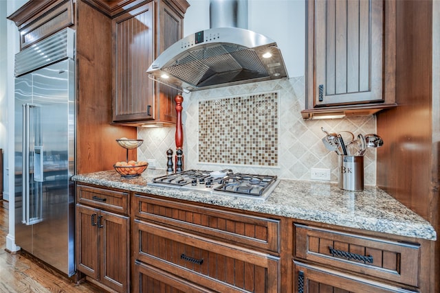 kitchen with stainless steel appliances, wall chimney range hood, light wood-style flooring, and light stone counters