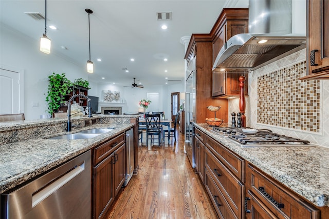 kitchen featuring visible vents, stainless steel appliances, ventilation hood, a fireplace, and a sink