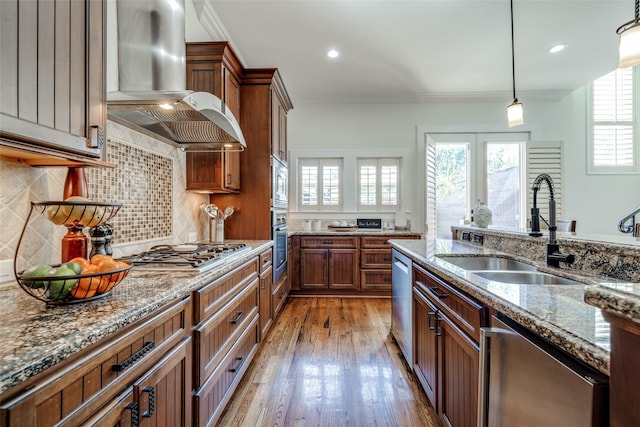 kitchen featuring brown cabinets, stainless steel appliances, a sink, wood finished floors, and exhaust hood