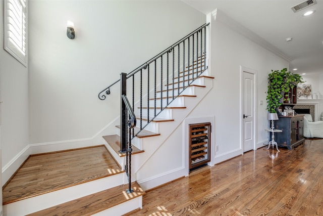 stairway with beverage cooler, baseboards, visible vents, wood finished floors, and a fireplace