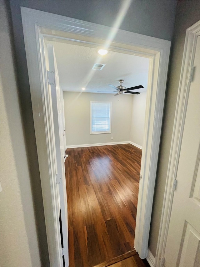 unfurnished room featuring dark wood-style flooring, visible vents, ceiling fan, and baseboards