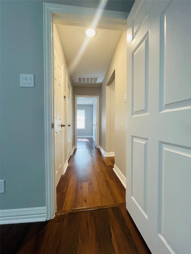 hall featuring wood finished floors, visible vents, and baseboards