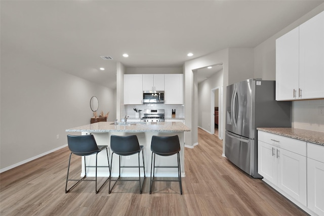 kitchen with visible vents, appliances with stainless steel finishes, light wood-style flooring, and a kitchen breakfast bar