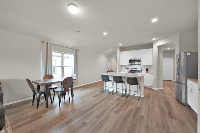 kitchen with stainless steel appliances, tasteful backsplash, visible vents, light wood-style floors, and white cabinets