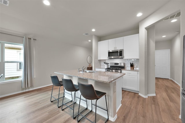 kitchen featuring stainless steel appliances, visible vents, decorative backsplash, light wood-style floors, and a kitchen island with sink