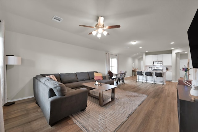 living room featuring visible vents, ceiling fan, light wood-style flooring, and baseboards