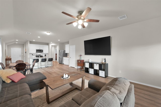 living area with light wood-style floors, visible vents, baseboards, and ceiling fan