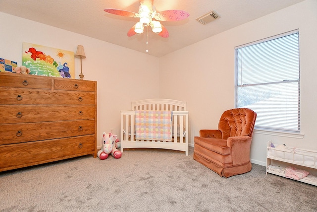 bedroom featuring a nursery area, visible vents, carpet, and a ceiling fan