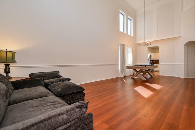 living room with baseboards, a chandelier, a towering ceiling, wood finished floors, and arched walkways