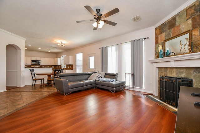 living area featuring arched walkways, visible vents, ornamental molding, and wood finished floors