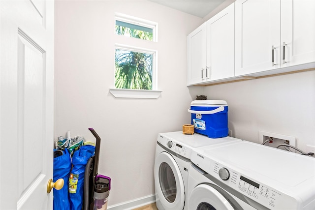 clothes washing area featuring washing machine and dryer, cabinet space, and baseboards