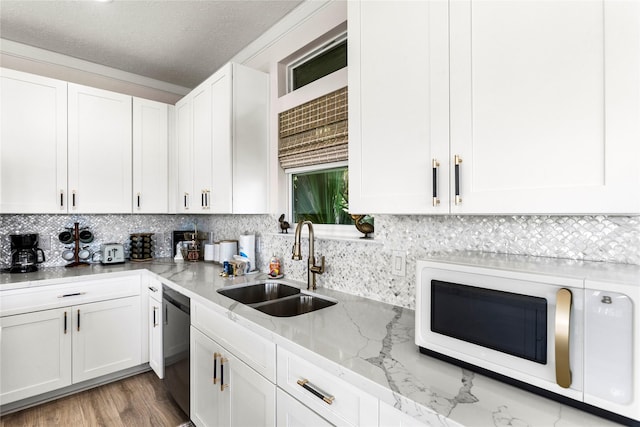 kitchen featuring white microwave, a sink, white cabinets, stainless steel dishwasher, and light stone countertops