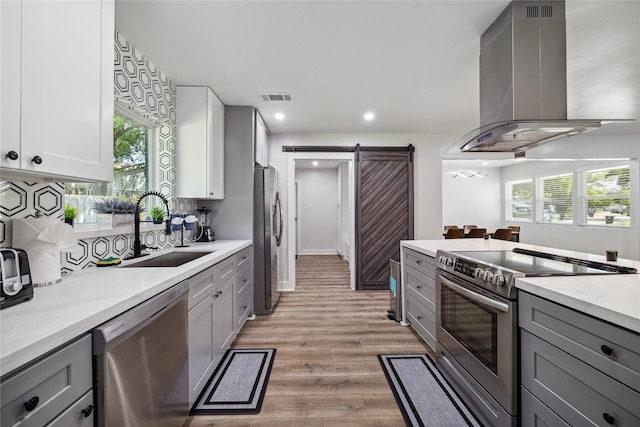 kitchen with stainless steel appliances, a barn door, wall chimney exhaust hood, and gray cabinetry