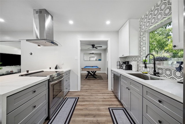 kitchen featuring light wood finished floors, island exhaust hood, gray cabinets, stainless steel appliances, and a sink