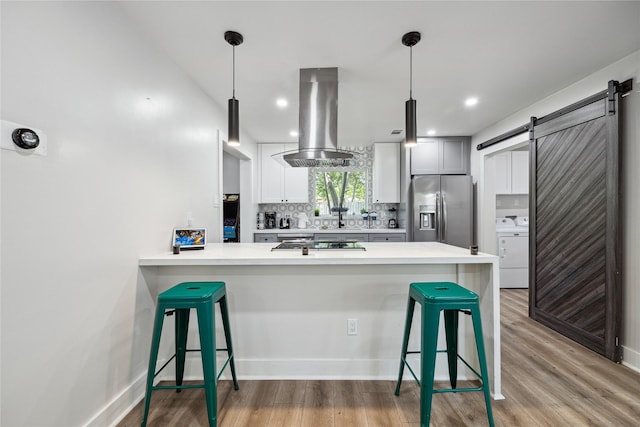 kitchen with a barn door, island range hood, decorative backsplash, stainless steel fridge with ice dispenser, and washer / clothes dryer