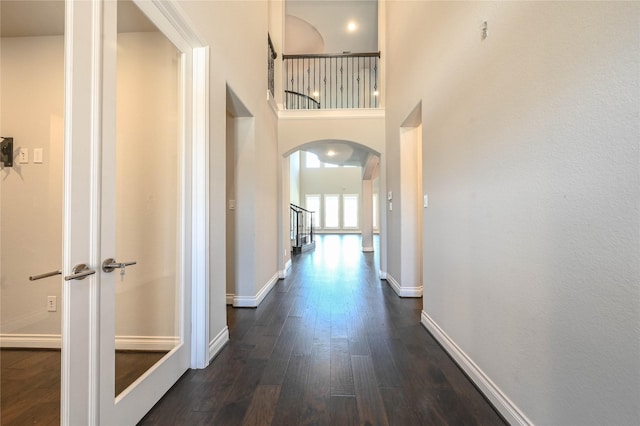 hall with dark wood-type flooring, arched walkways, a high ceiling, and baseboards