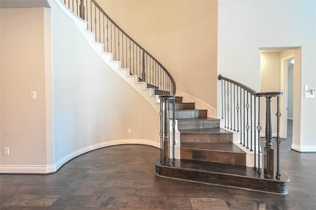 stairway with a high ceiling, baseboards, and wood finished floors