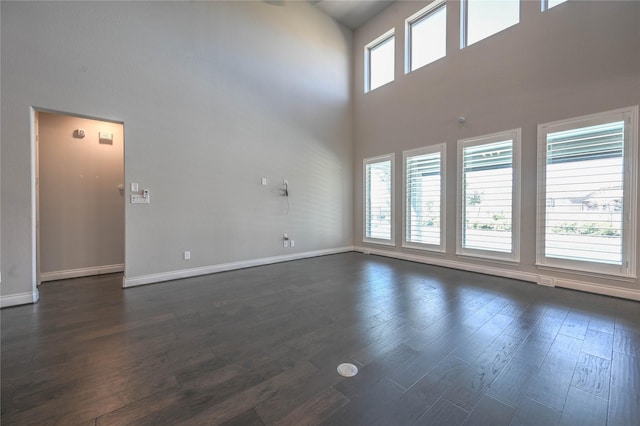 spare room featuring dark wood-type flooring, a towering ceiling, and baseboards