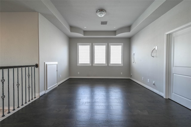 empty room with dark wood-style flooring, visible vents, and baseboards