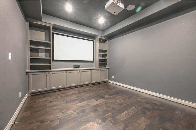 home theater room with a tray ceiling, dark wood-type flooring, and baseboards