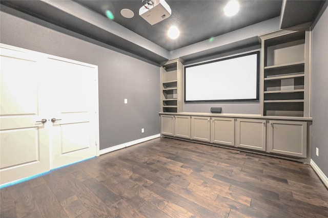 home theater with a tray ceiling, dark wood-type flooring, and baseboards