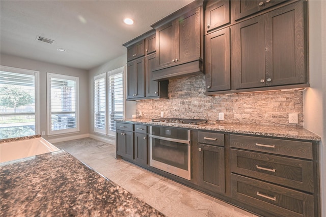 kitchen with tasteful backsplash, visible vents, appliances with stainless steel finishes, dark brown cabinets, and premium range hood