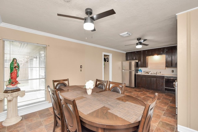 dining room featuring visible vents, a textured ceiling, ornamental molding, and a ceiling fan