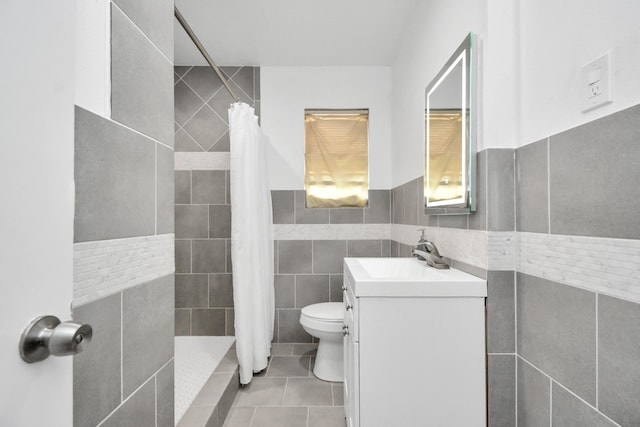 bathroom featuring tile patterned flooring, toilet, vanity, tile walls, and tiled shower