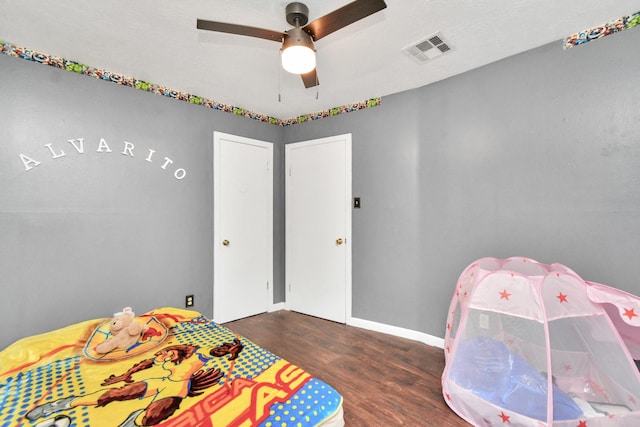 bedroom with a ceiling fan, visible vents, baseboards, and wood finished floors