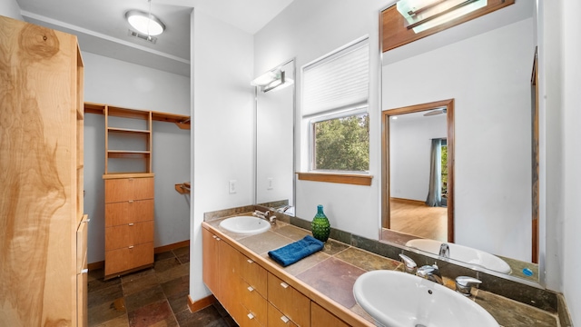 bathroom with a sink, visible vents, stone tile floors, and double vanity