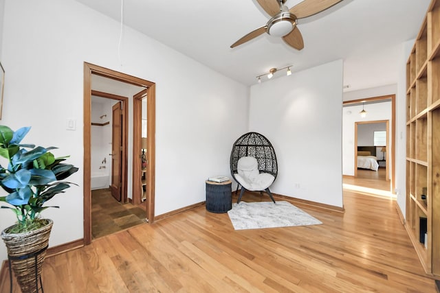 living area featuring light wood finished floors, attic access, baseboards, and a ceiling fan