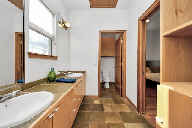 bathroom featuring double vanity, toilet, baseboards, and a sink