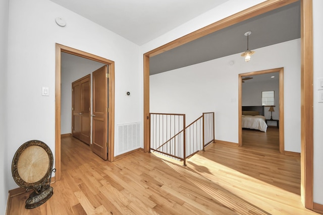 hallway with an upstairs landing, visible vents, light wood finished floors, and baseboards