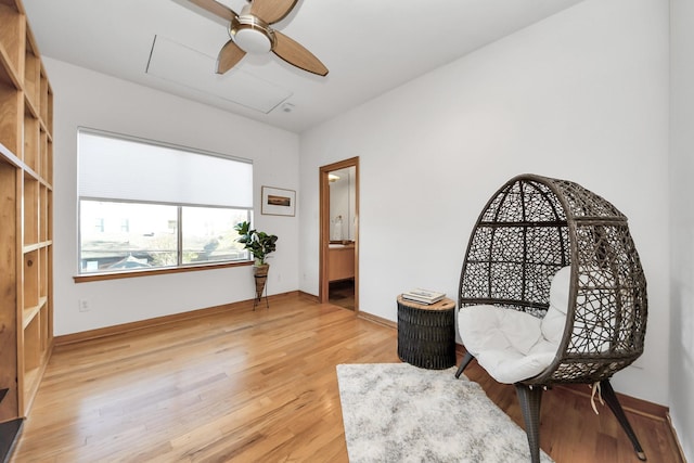 sitting room featuring attic access, ceiling fan, baseboards, and light wood-style floors