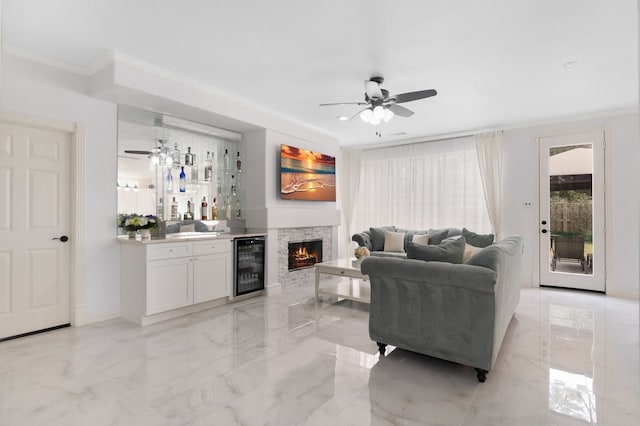 living area featuring ceiling fan, beverage cooler, marble finish floor, and ornamental molding