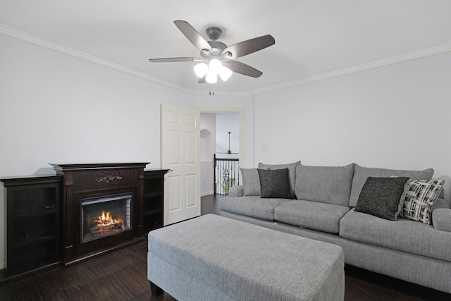 living room featuring ornamental molding, a warm lit fireplace, ceiling fan, and dark wood-style flooring