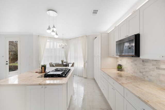 kitchen with a notable chandelier, marble finish floor, black gas cooktop, stainless steel microwave, and a center island