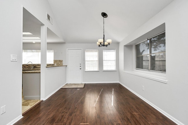 unfurnished dining area with lofted ceiling, visible vents, wood finished floors, a chandelier, and baseboards