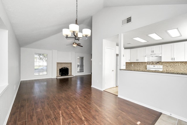 unfurnished living room with baseboards, visible vents, wood finished floors, a fireplace, and ceiling fan with notable chandelier