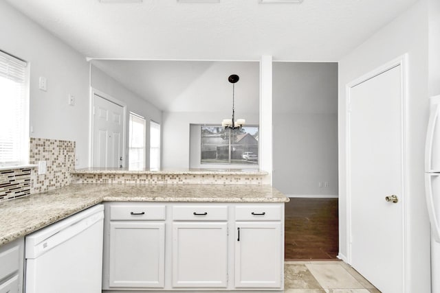 kitchen featuring white dishwasher, a peninsula, white cabinets, backsplash, and an inviting chandelier