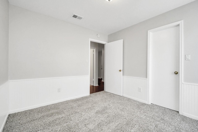 unfurnished bedroom with a wainscoted wall, visible vents, and carpet flooring