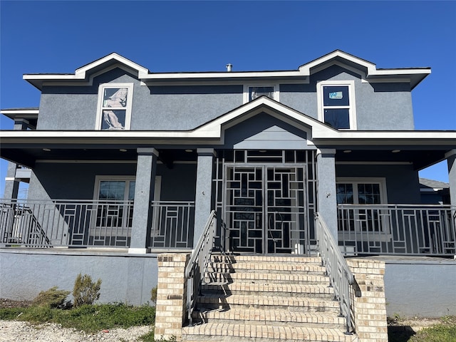 view of front of house with a porch, stairway, and stucco siding