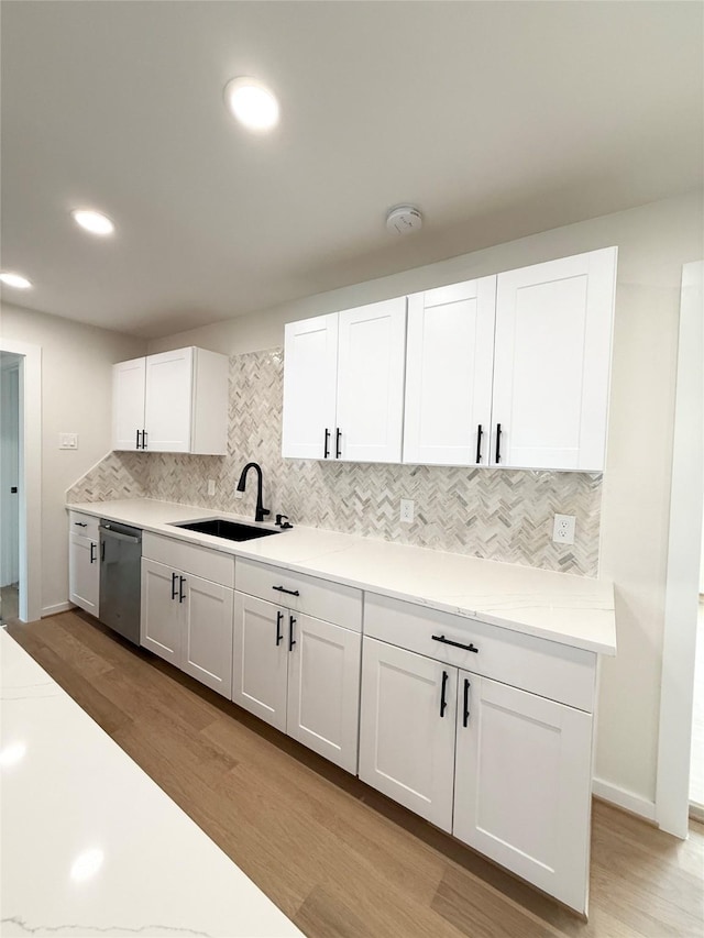 kitchen with light wood-style flooring, a sink, white cabinetry, light countertops, and stainless steel dishwasher