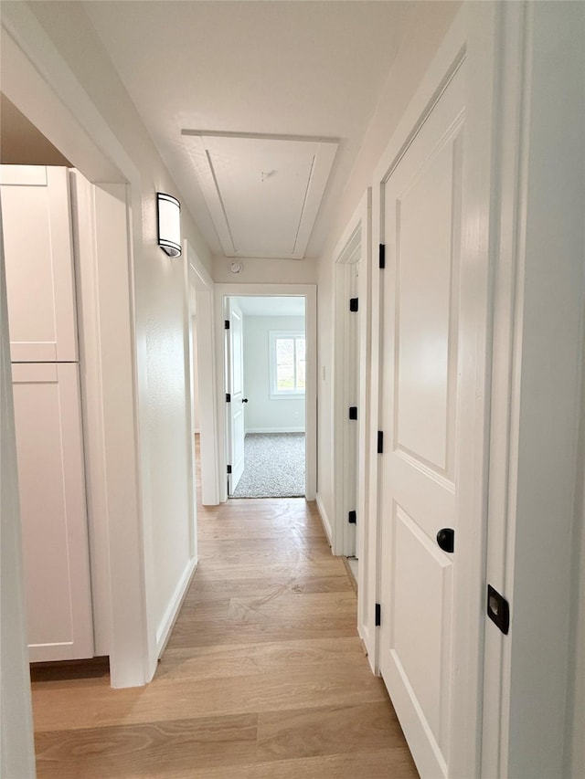 corridor with attic access, light wood-style floors, and baseboards