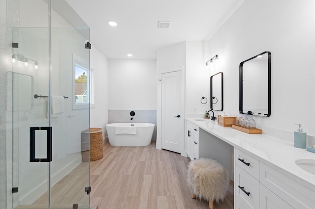 bathroom with double vanity, a stall shower, a soaking tub, wood finished floors, and a sink