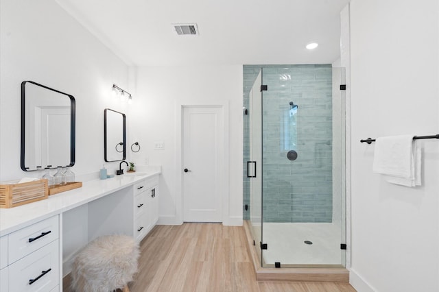 full bath with double vanity, a stall shower, visible vents, wood finished floors, and a sink