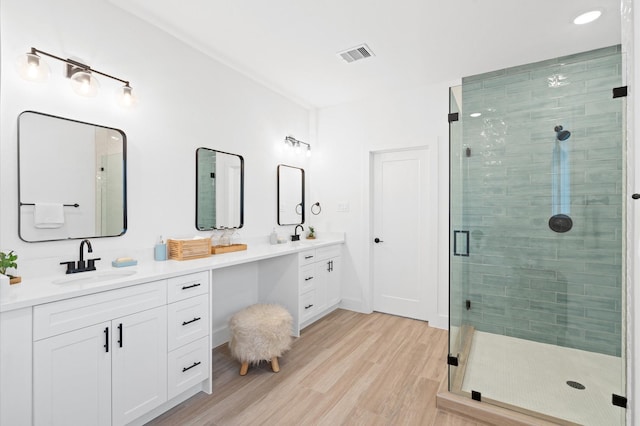 full bath with double vanity, a stall shower, visible vents, wood finished floors, and a sink