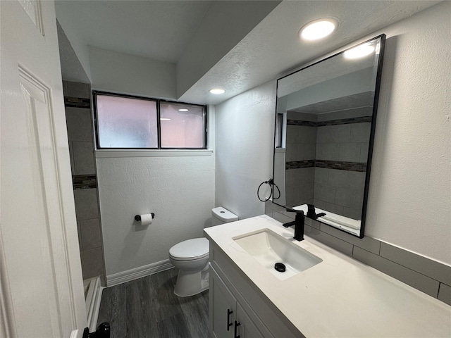 full bathroom with toilet, vanity, wood finished floors, tiled shower, and baseboards