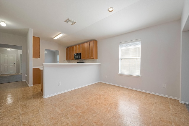 kitchen with brown cabinets, light countertops, black microwave, and visible vents