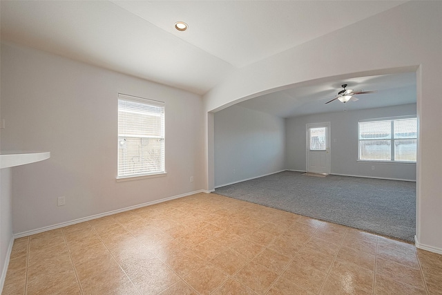 empty room with light carpet, baseboards, arched walkways, a ceiling fan, and lofted ceiling